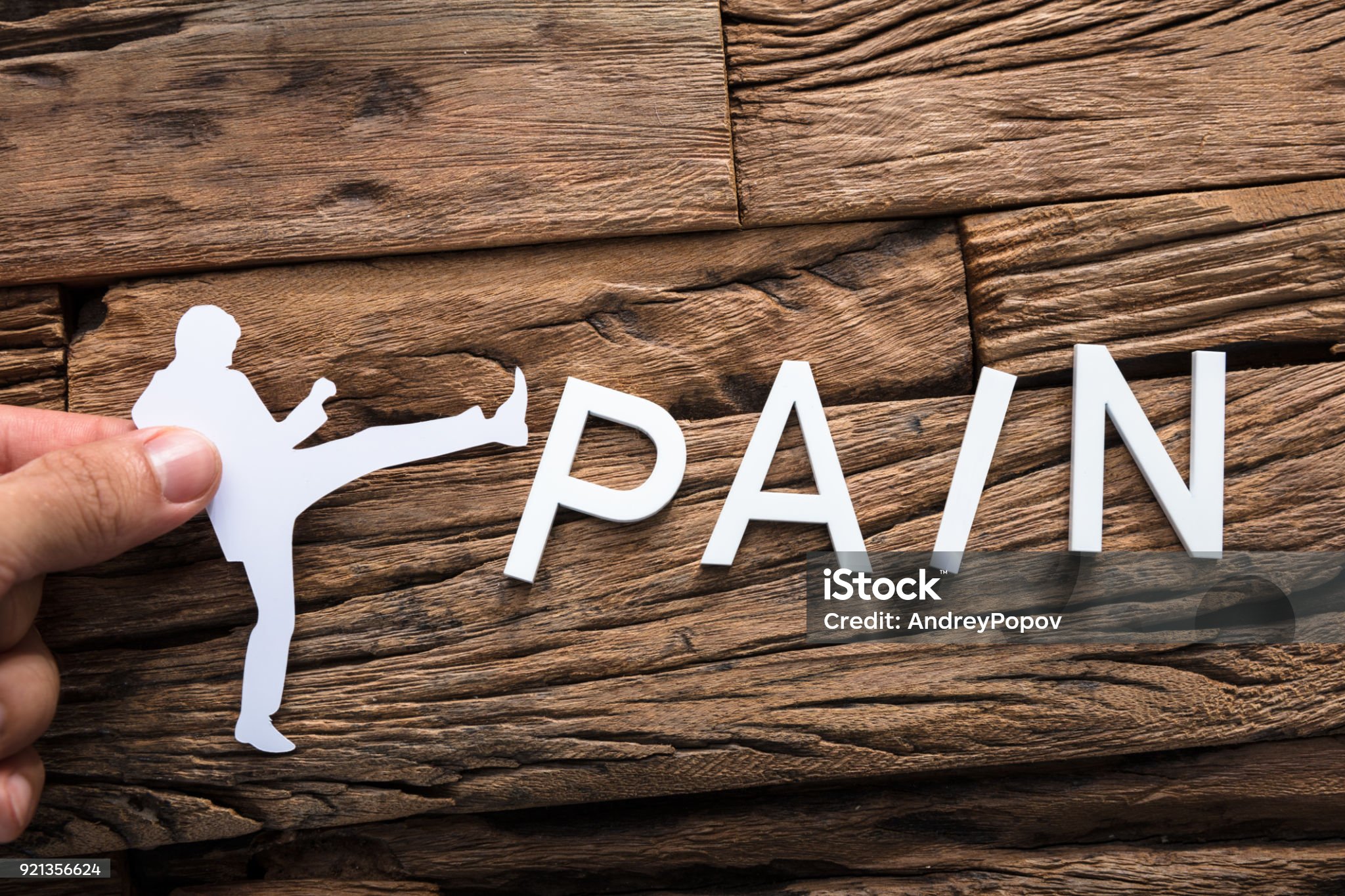 Closeup of hand holding paper businessman kicking word pain on wood